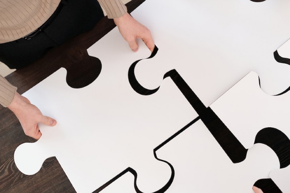 Neljä suurta palapelin palaa ja kädet, jotka asettelevat paloja paikoilleen